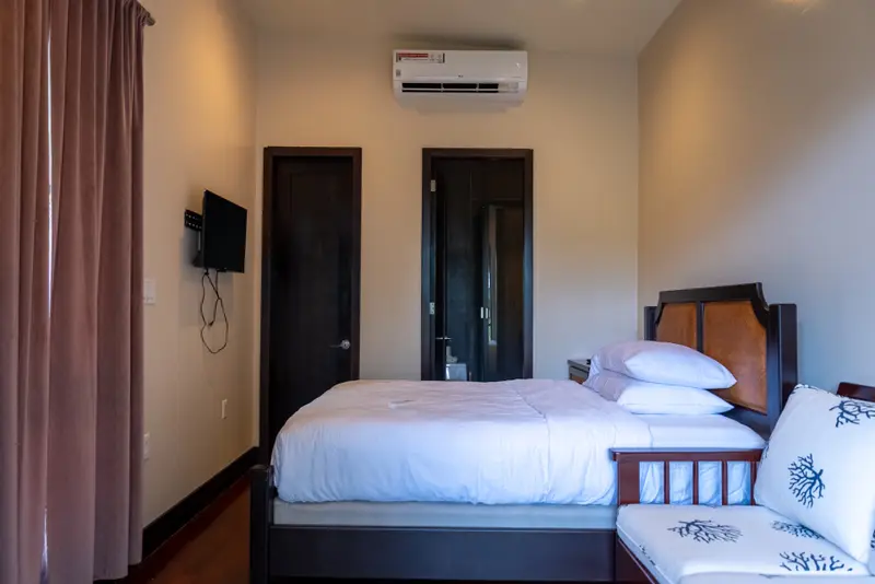 Bedroom with white bed linen, wall-mounted air conditioner and dark wood doors