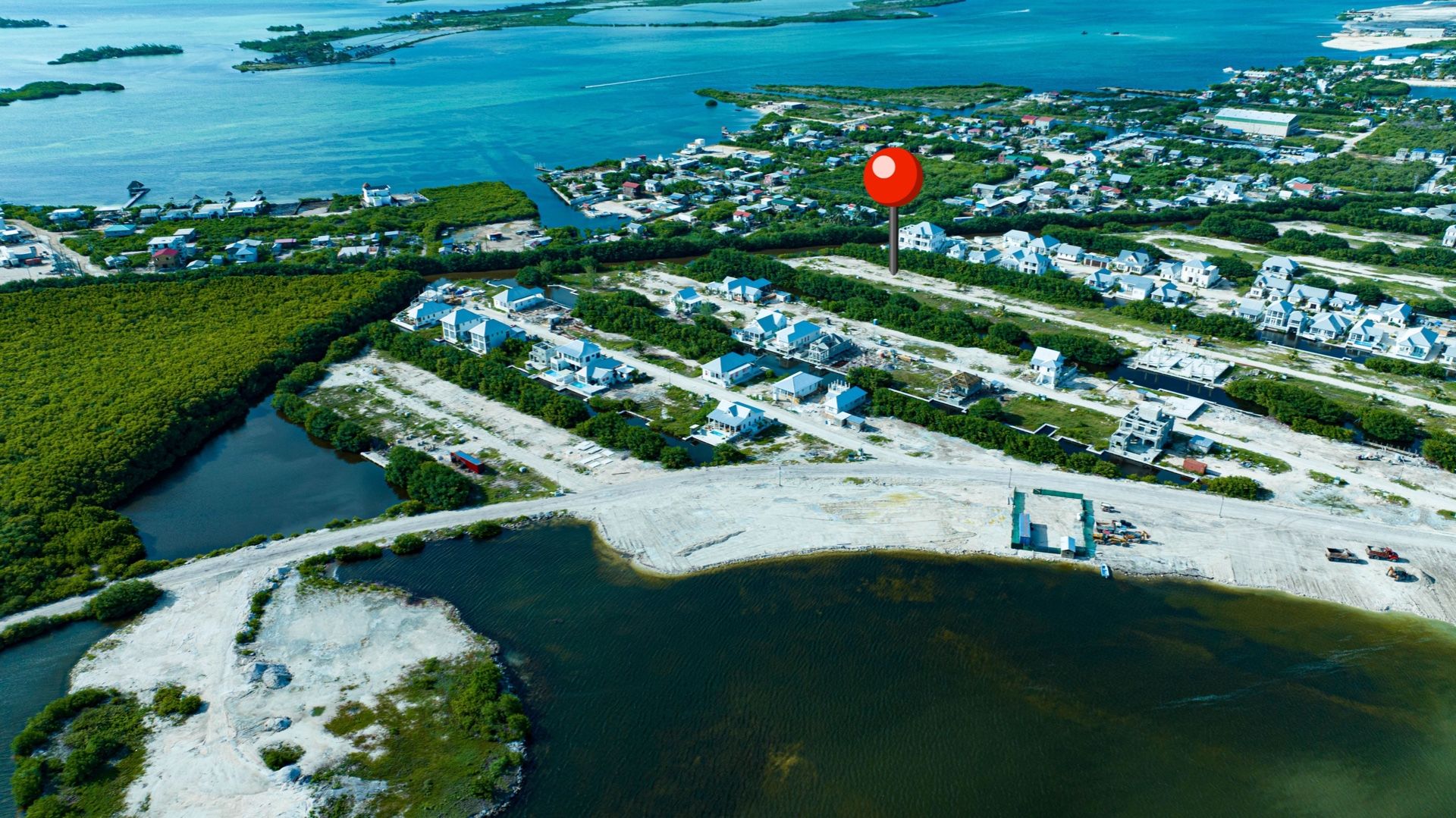 Aerial view of cleared waterfront lots beside white-roofed houses and mangroves