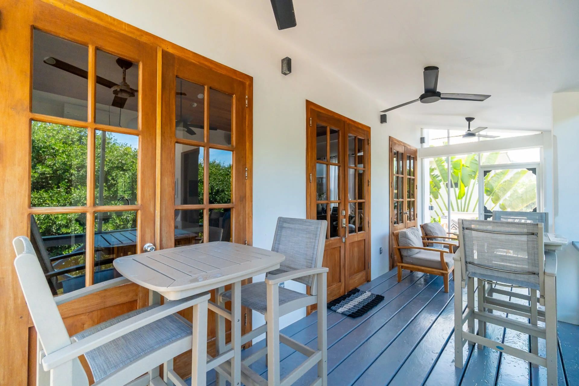 Covered porch with grey bar table, tall chairs and wood-framed French doors