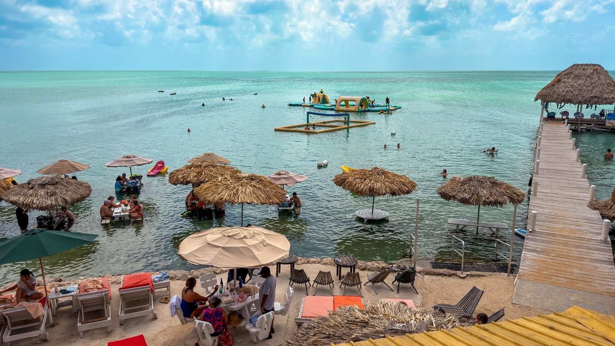 Shallow turquoise water with inflatable water park and thatched umbrellas on the shore
