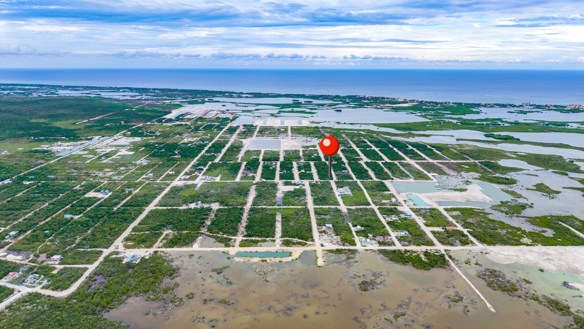 Aerial view of a gridded lot subdivision with scrub vegetation and sea beyond