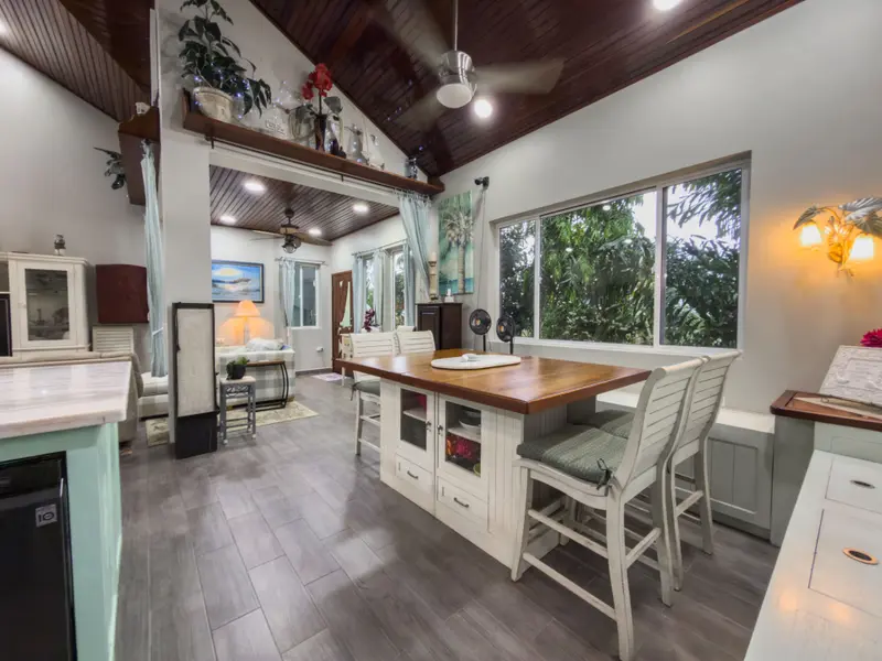 Open kitchen island with wood countertop, white cabinets and green-cushioned stools