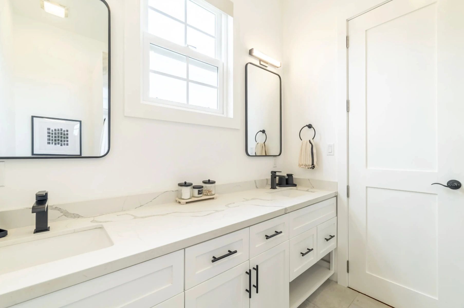 Bathroom vanity with white shaker cabinets, marble-look countertop and black hardware