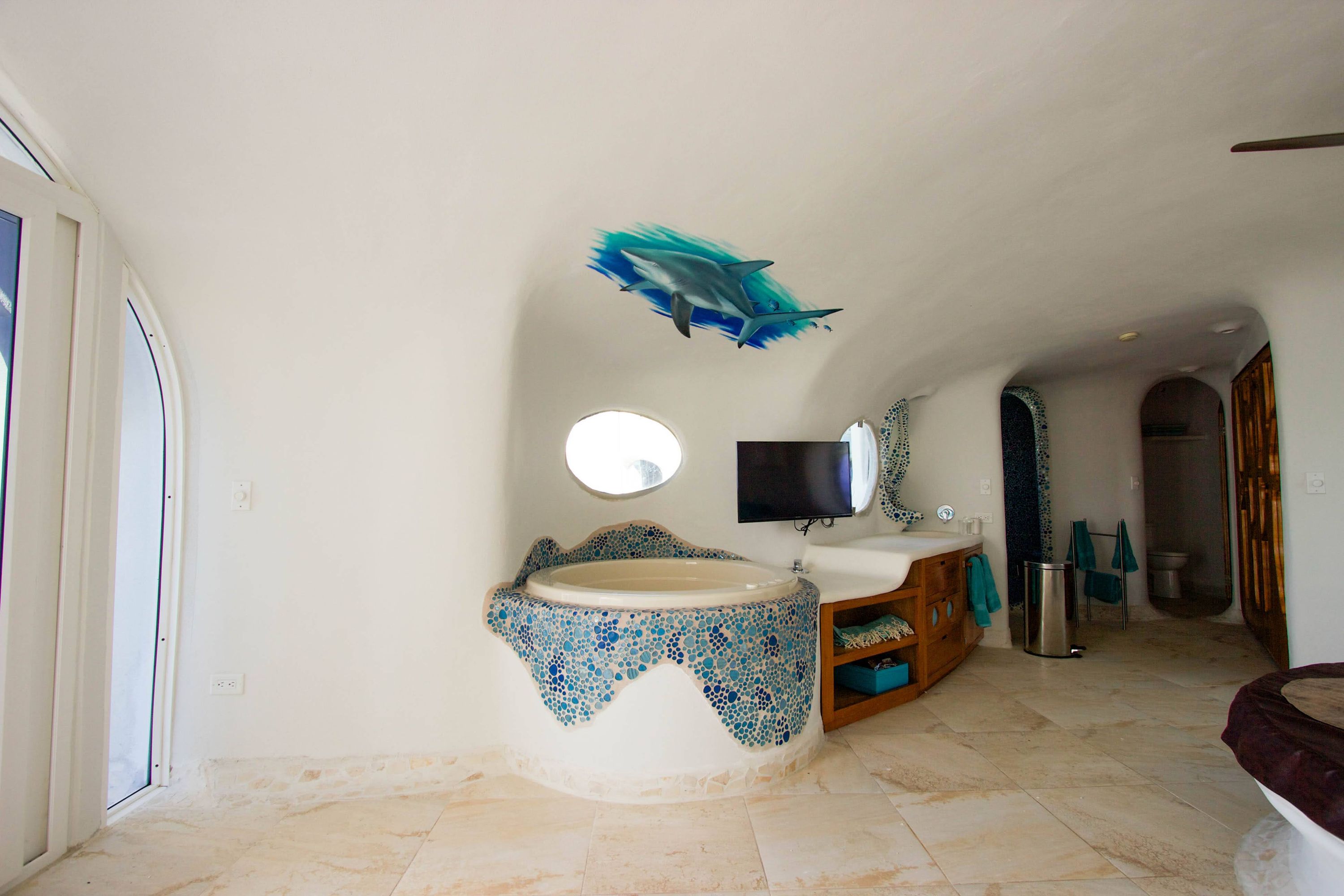 Round soaking tub with blue mosaic tile and a painted shark mural above