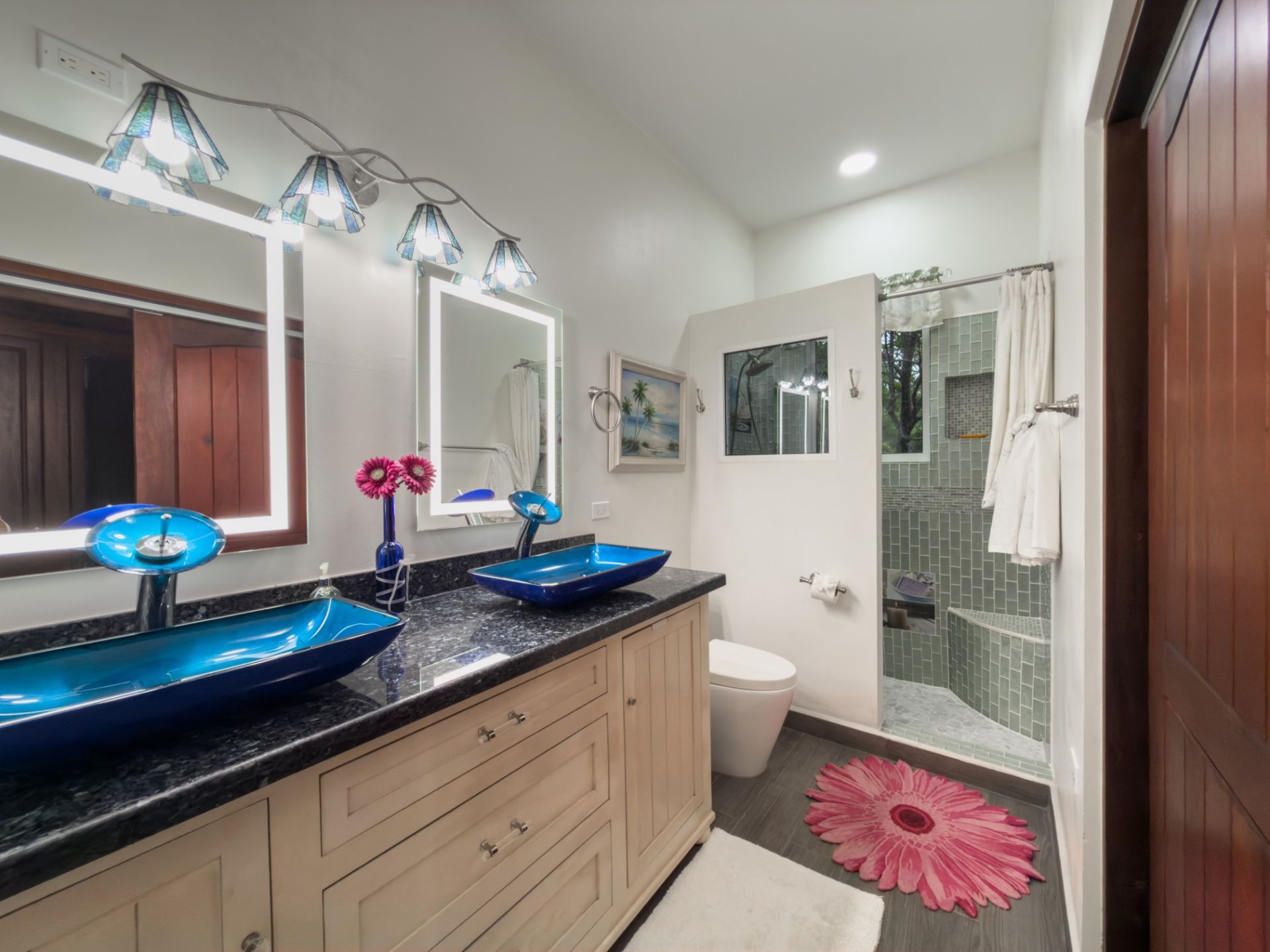 Bathroom with blue glass vessel sink and light wood vanity under a lit mirror