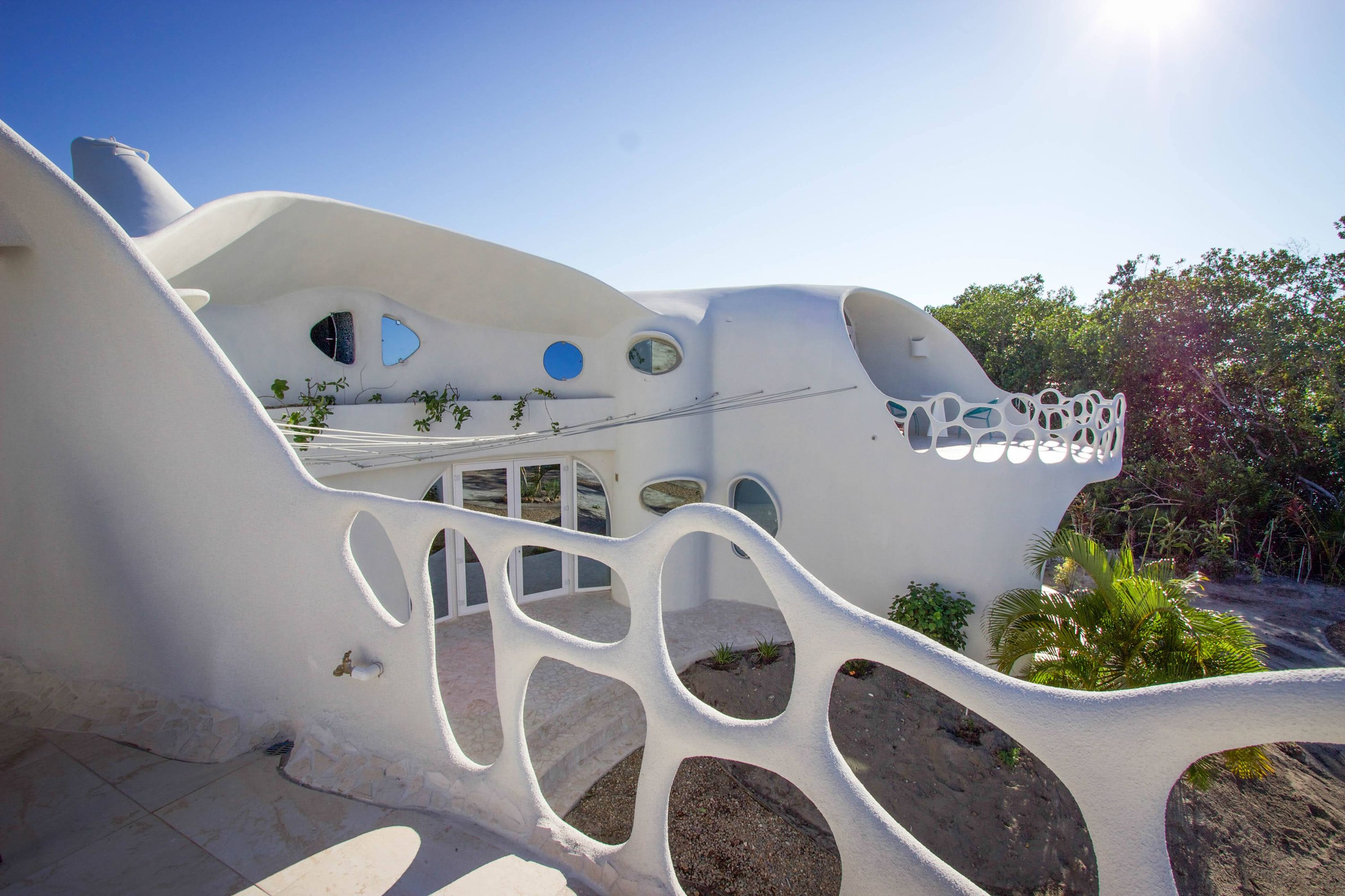 Curved white stucco facade with round porthole windows and an openwork wall