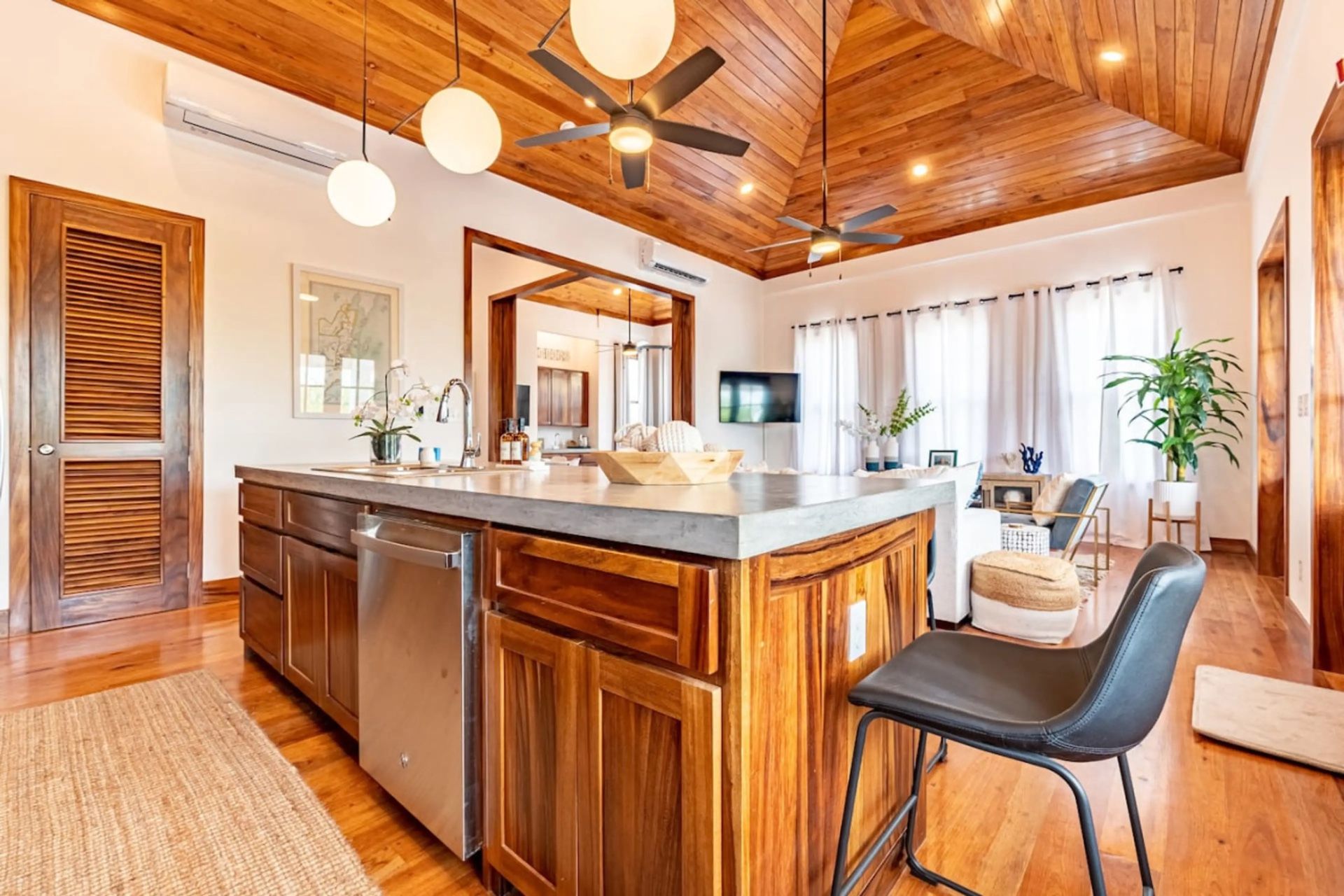Kitchen island with concrete countertop, wood cabinets and black barstool beneath wood ceiling
