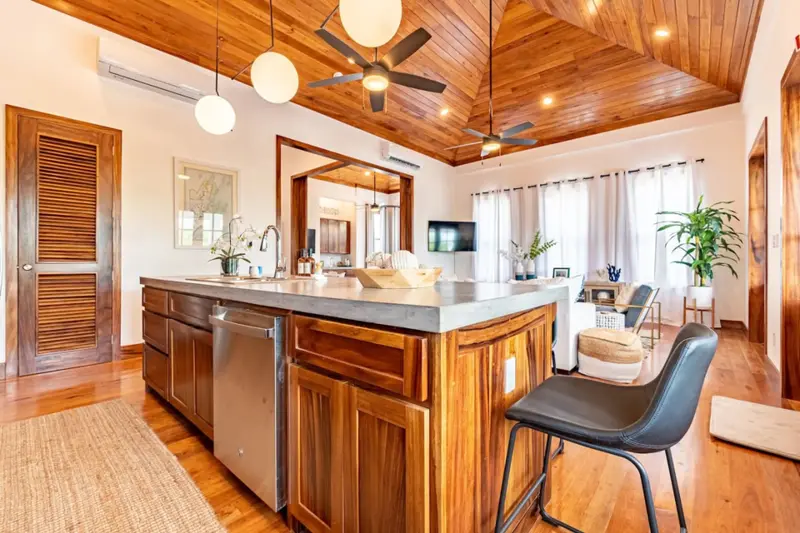 Kitchen island with concrete countertop, wood cabinets and black barstool beneath wood ceiling