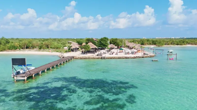 Aerial view of thatched beach huts and umbrellas on sand beside turquoise water