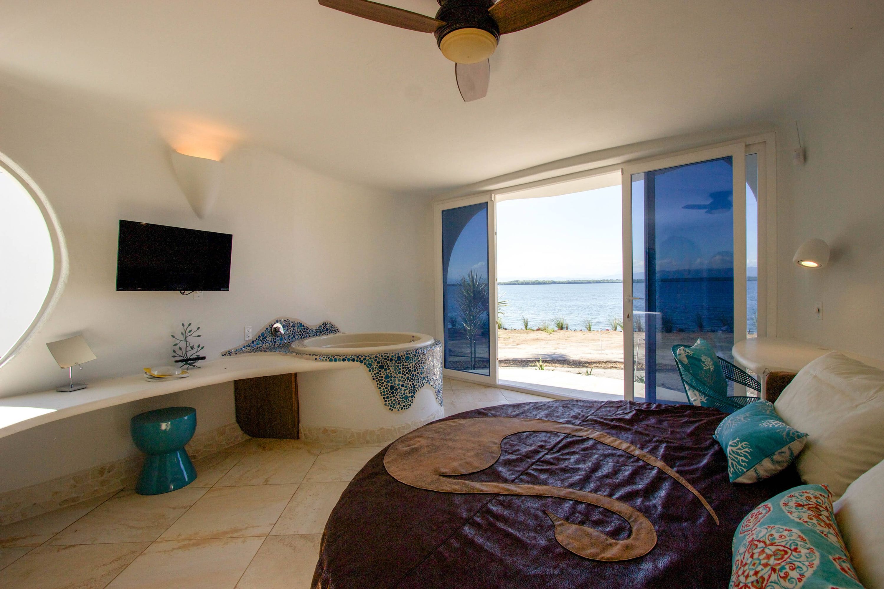 Round bed with dark leather cover beside mosaic tiled tub and water view