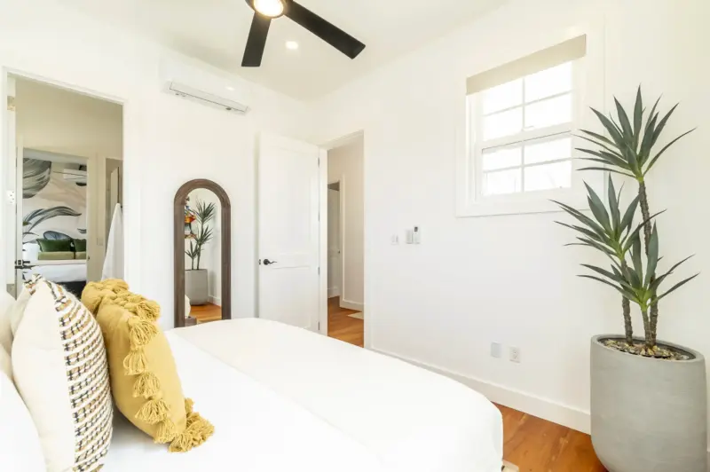 Bedroom with white bed, black ceiling fan and hardwood hallway beyond