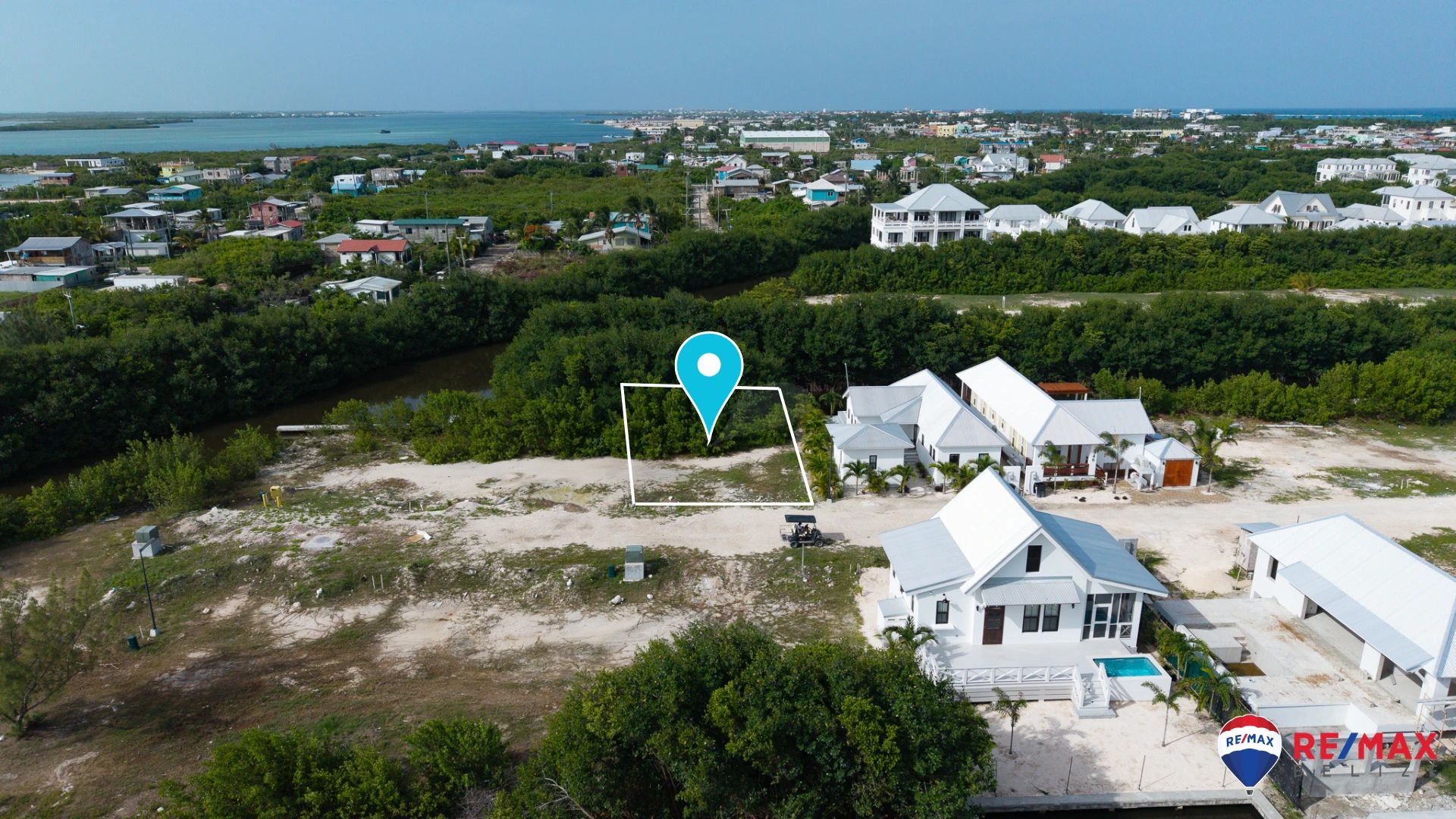 Aerial view of vacant lot outlined in white with map pin, neighboring white houses beside