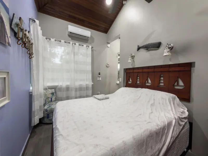 Bedroom with white bed, wooden headboard with sailboat carvings and wood-paneled ceiling