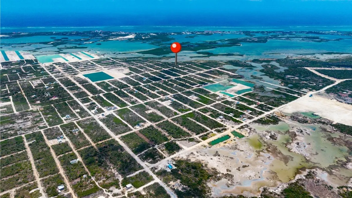Aerial view of subdivided lots with dirt roads and turquoise water beyond