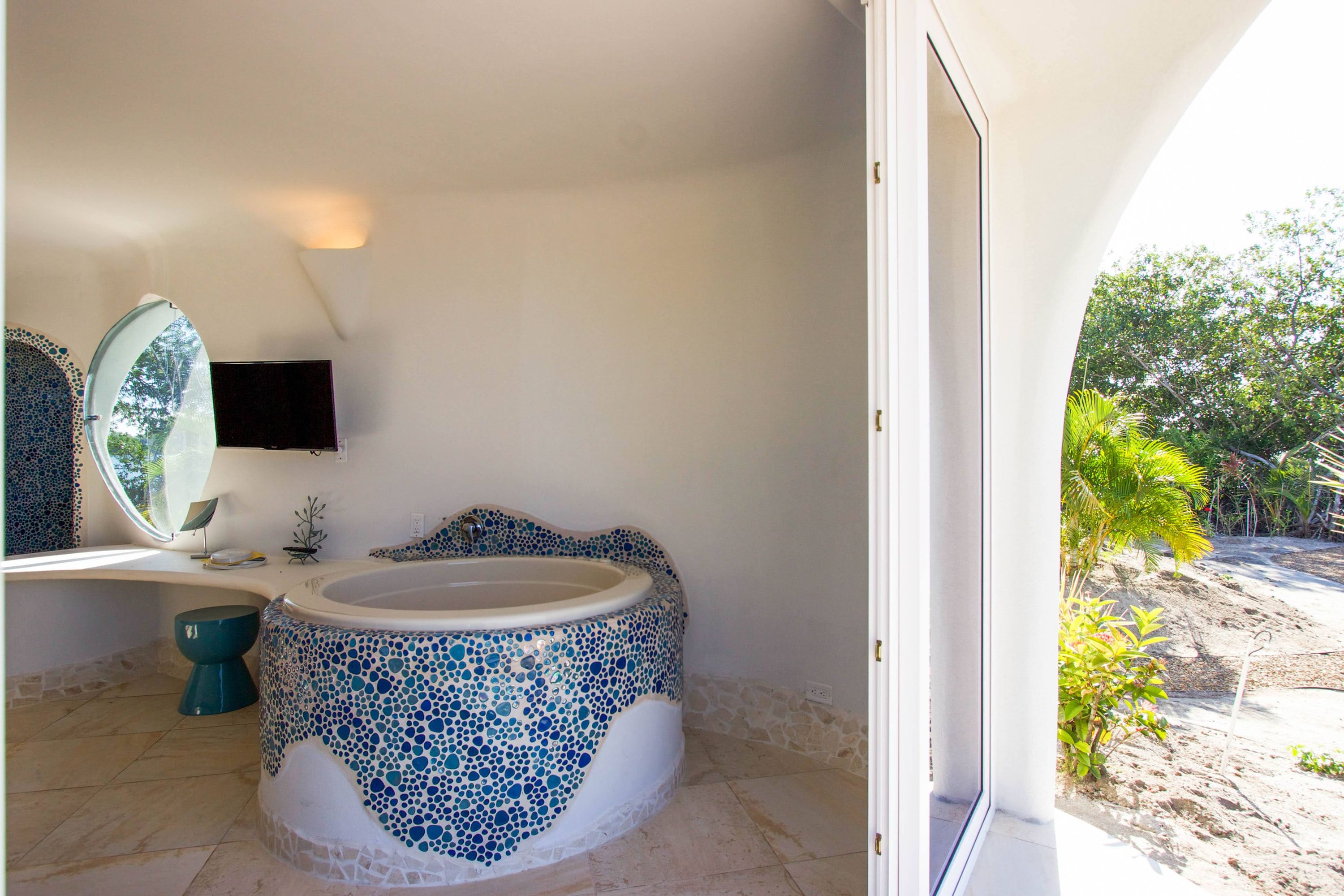 Bathtub with blue pebble mosaic tile border beside beige stone floor