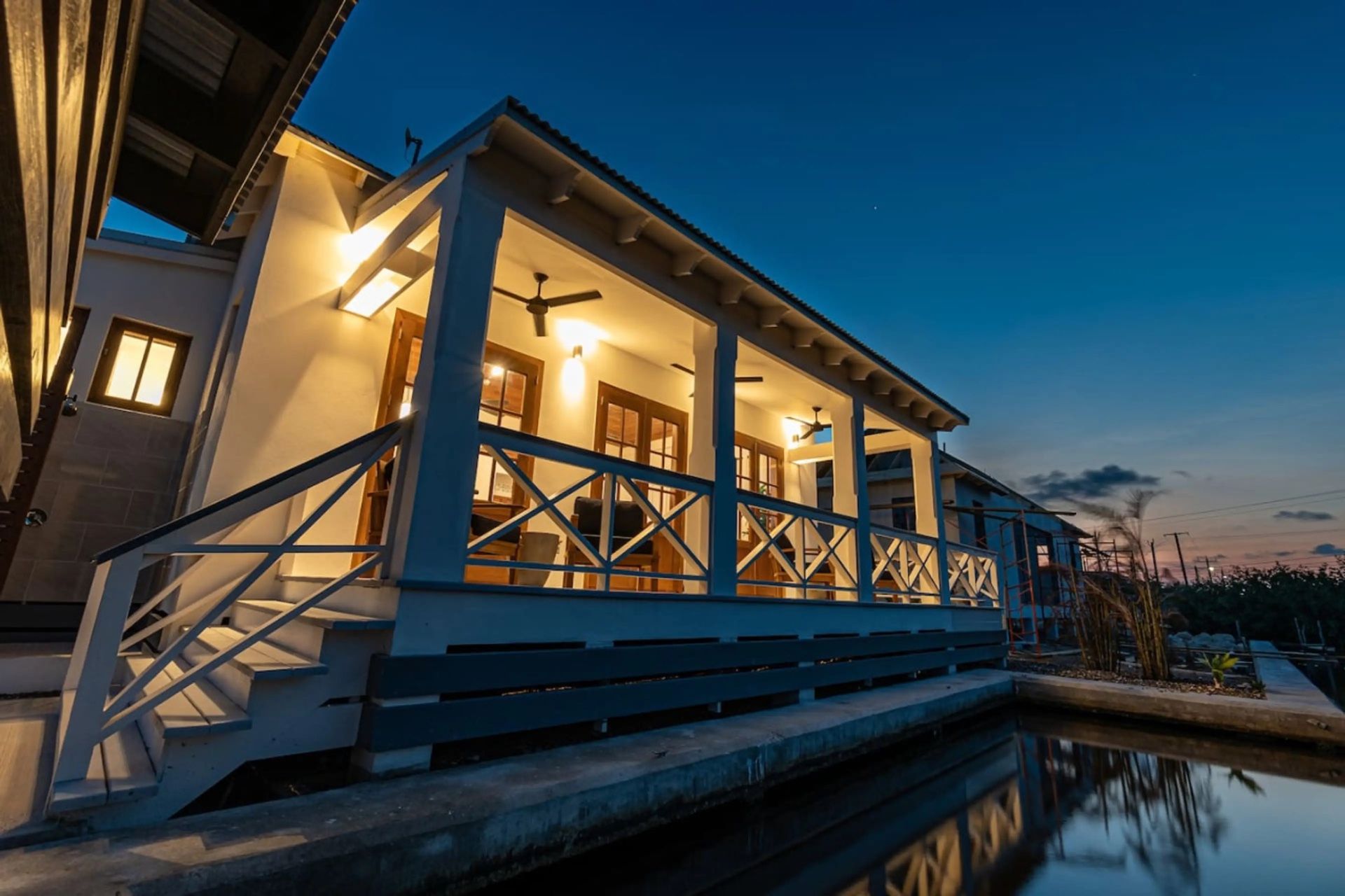 Dusk view of a covered porch with ceiling fans and lit French doors