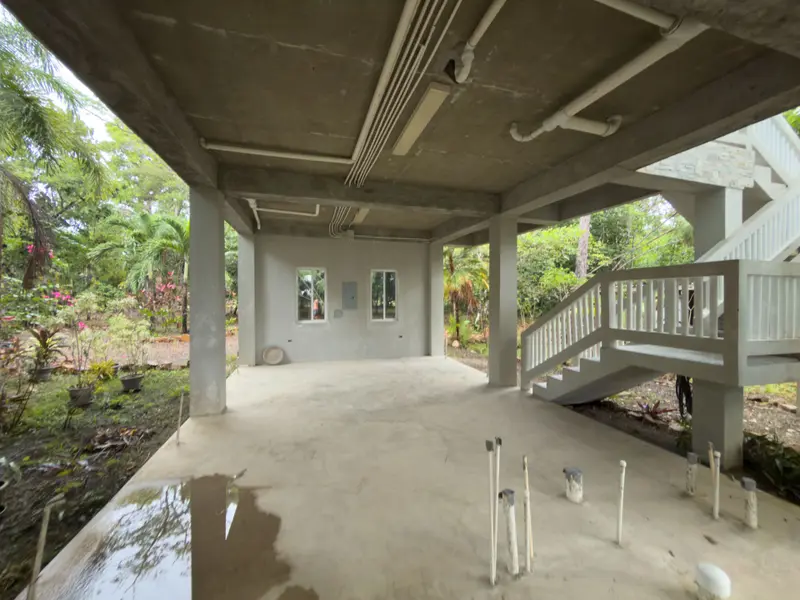 Unfinished open ground floor with bare concrete ceiling, exposed pipes and plastered walls