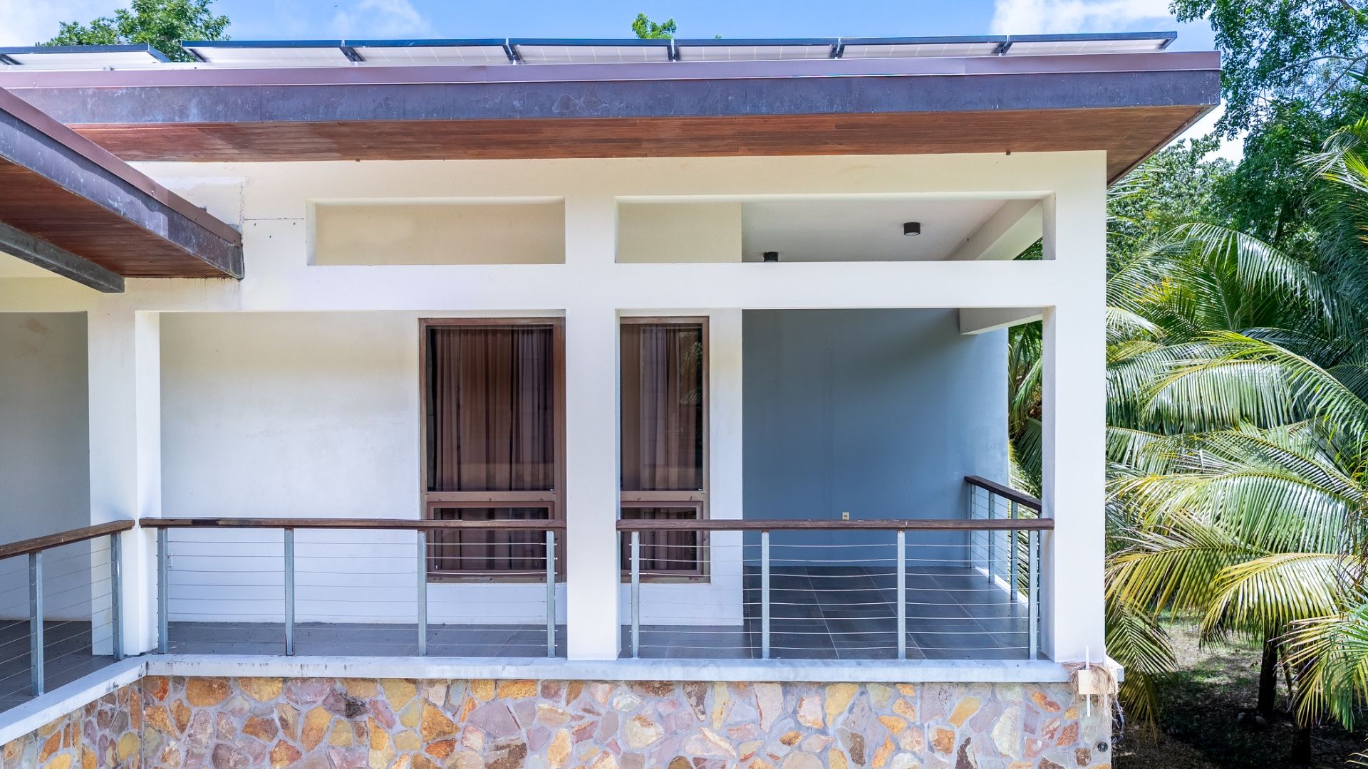 Covered terrace with wood-framed windows, cable railing and stone base