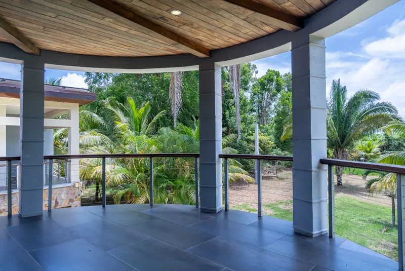 Covered deck with dark tile floor, wood ceiling and cable railing over palm trees