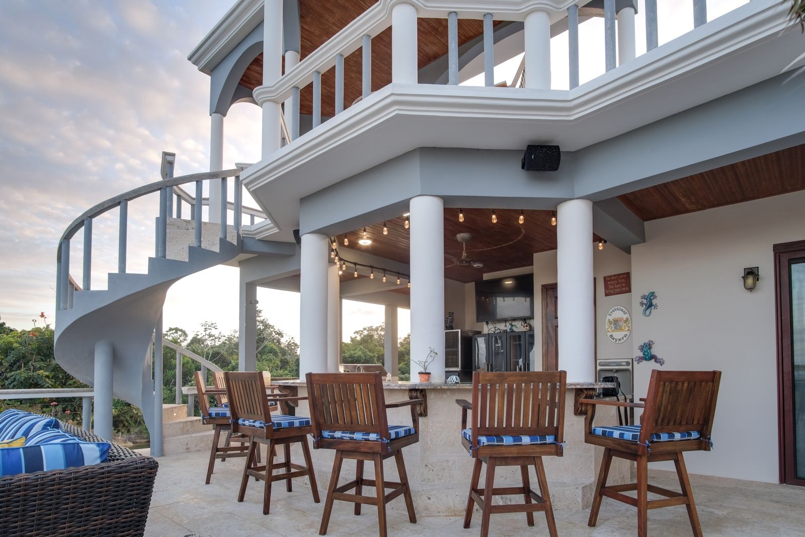 Covered outdoor bar with wooden swivel stools, blue cushions and string lights