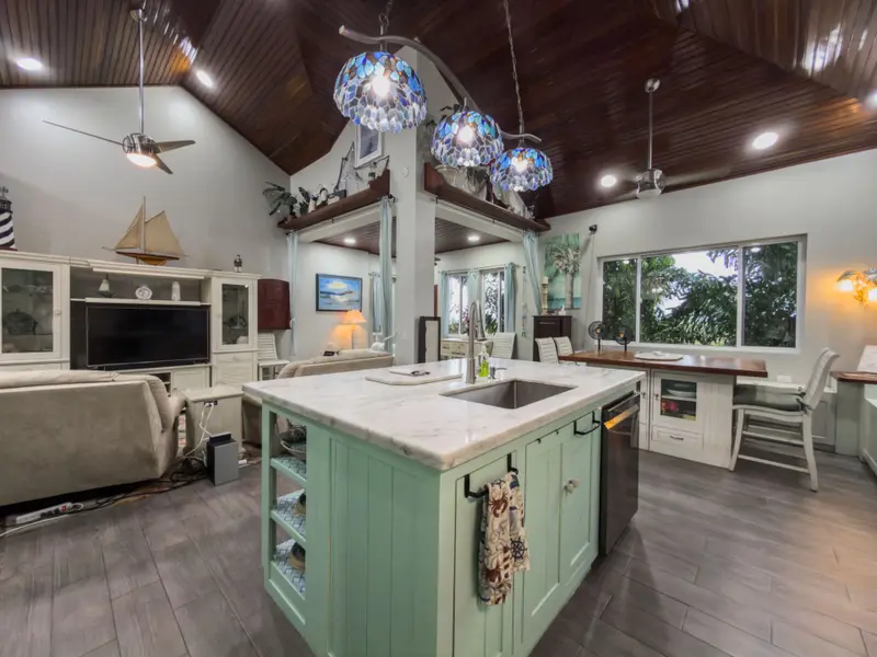 Kitchen island with marble top, sink and mint green cabinets under blue glass pendant lights