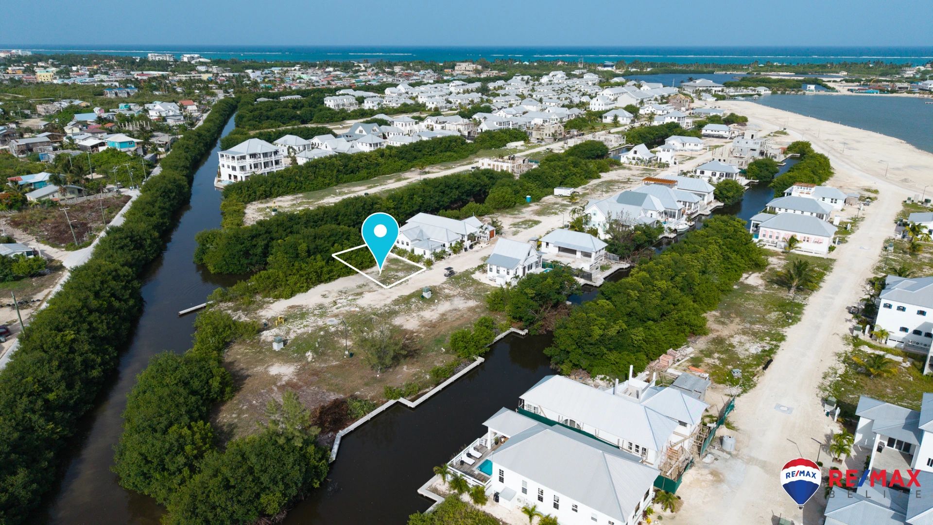 Aerial view of a vacant lot outlined in white beside a canal with white roofed homes