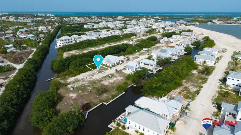 Aerial view of a vacant lot outlined in white beside a canal with white roofed homes