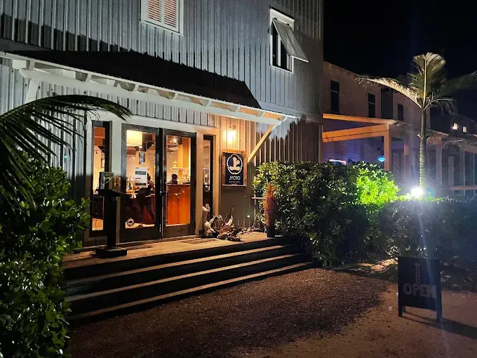 Evening view of a grey clapboard building entrance with glass doors and palm trees