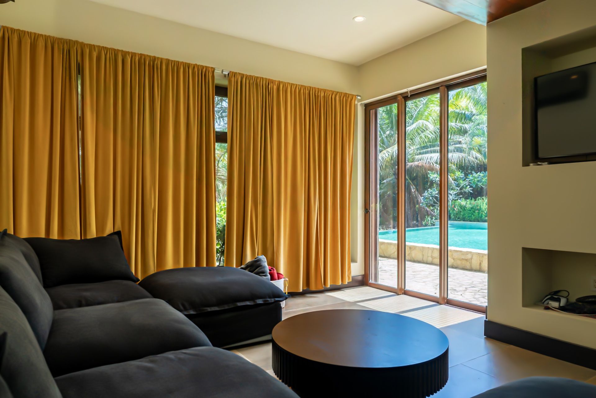 Living room with mustard curtains, dark sofa and round black coffee table