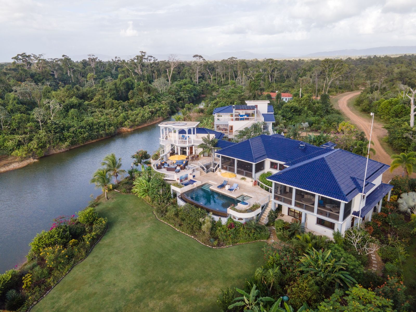 Aerial view of white villa with blue roofs beside a pool and river