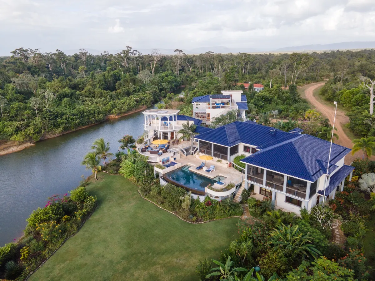 Aerial view of white villa with blue roofs beside a pool and river