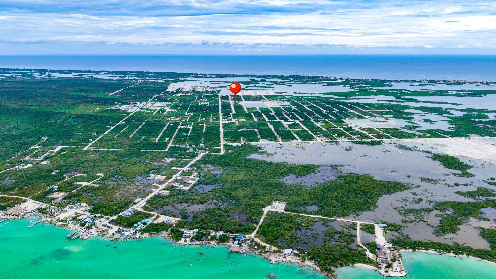 Aerial view of gridded land parcels with red location pin above flooded mangrove and turquoise water