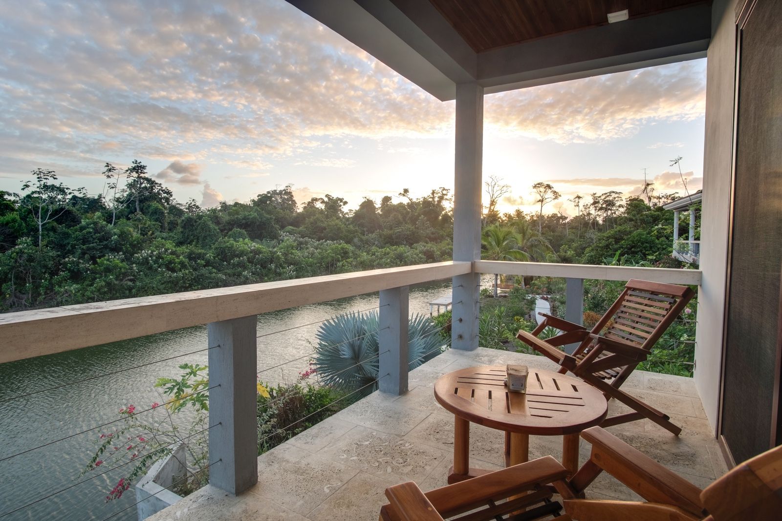 Covered balcony with wooden side table and chairs overlooking a calm river at sunset
