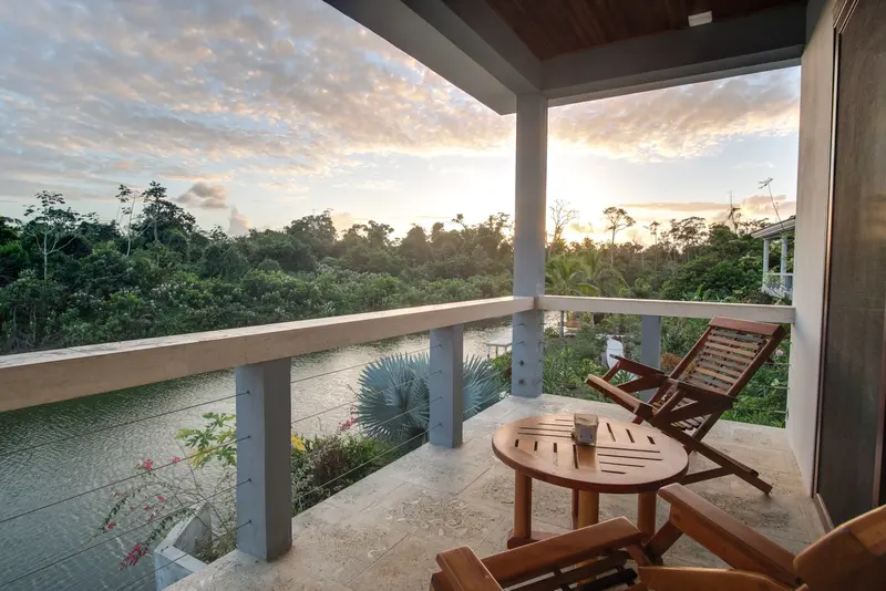 Covered balcony with wooden side table and chairs overlooking a calm river at sunset