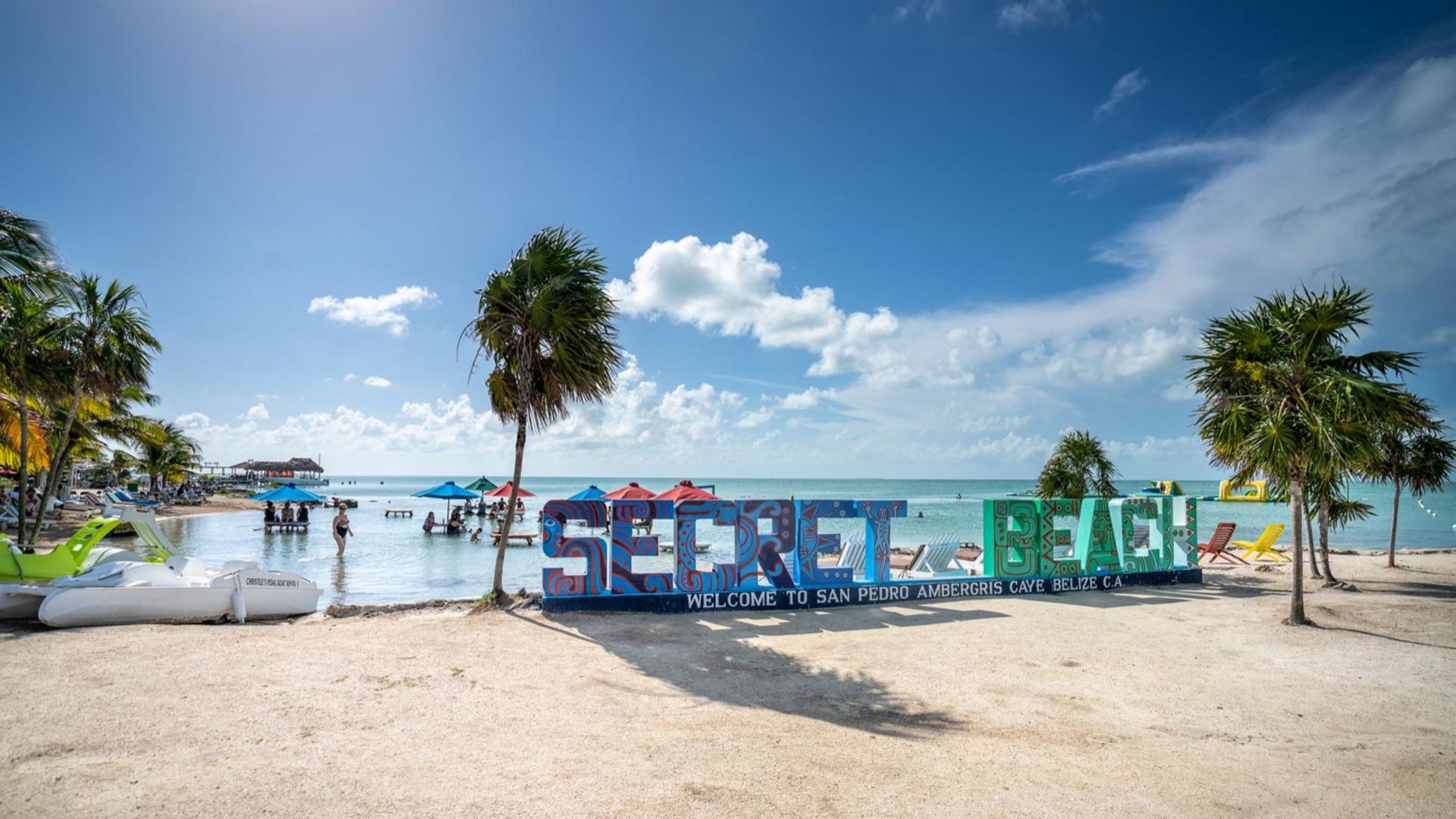 Large painted sign spelling secret beside sea, palm tree and sandy beach