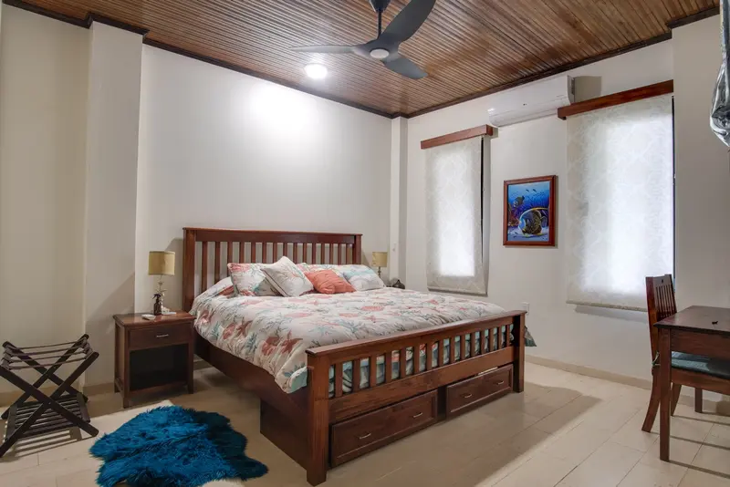 Bedroom with wood-slat bed, coral floral bedding and wood-paneled ceiling