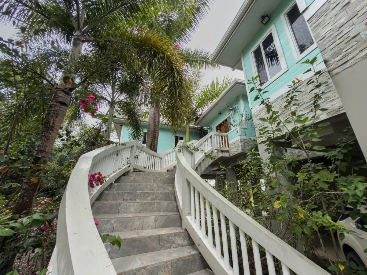 Stone staircase with white railings leading past turquoise house and palm trees