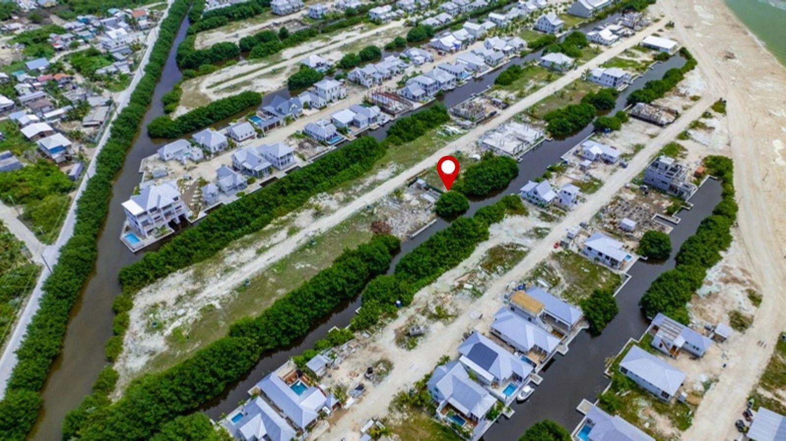 Aerial view of a vacant canal-side lot marked with a red pin, bordered by mangroves