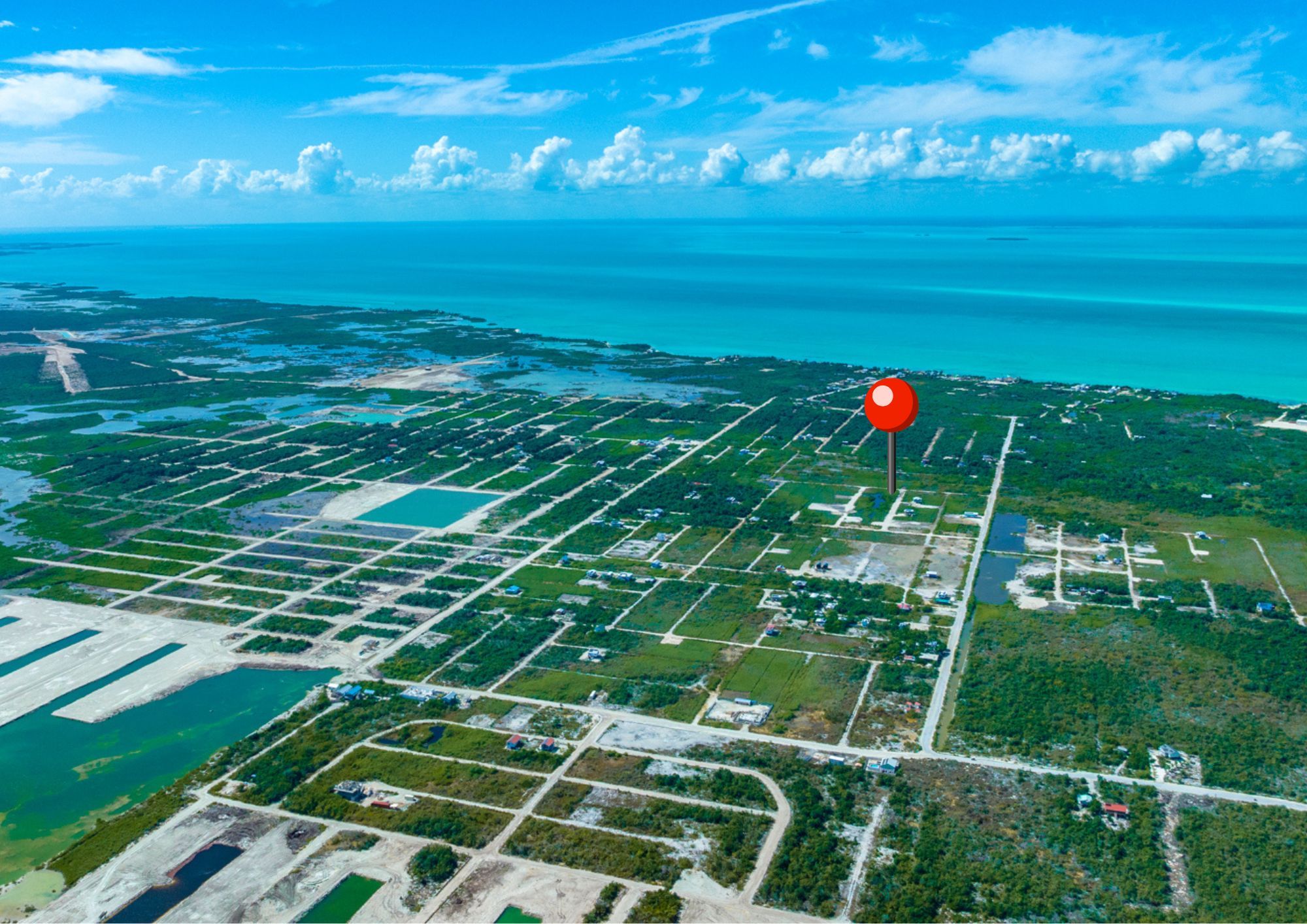 Aerial view of gridded residential lots along turquoise coastline with red location pin