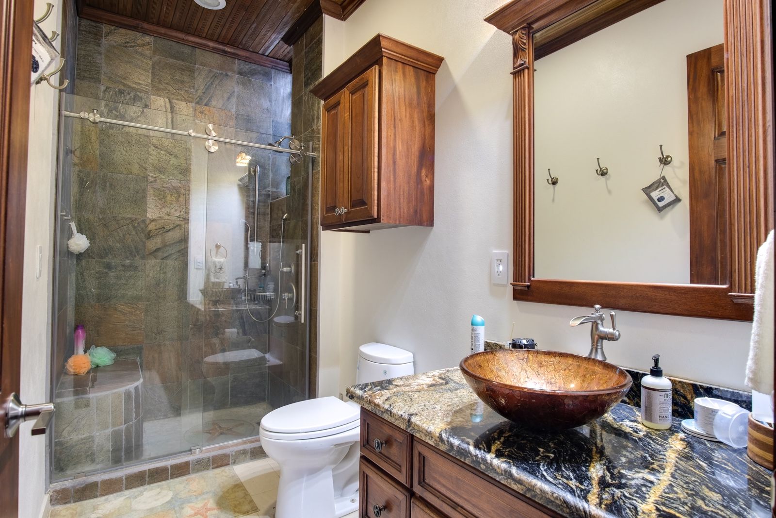 Bathroom with glass-enclosed shower, wood wall cabinet and vessel sink on granite