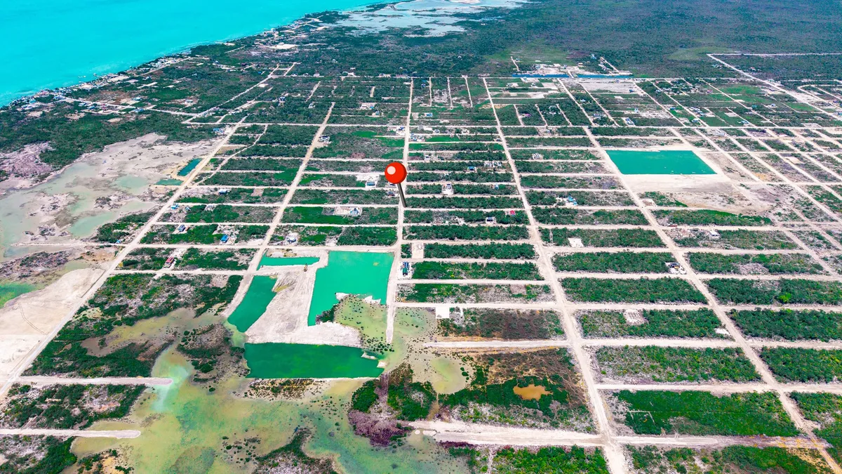 Aerial view of gridded land lots with scattered scrub, dirt roads and turquoise ponds