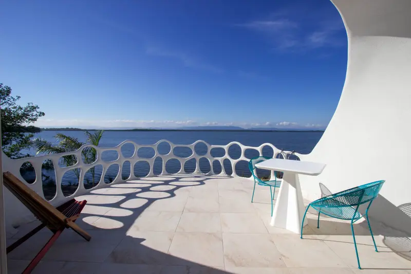 Terrace with white sculptural railing overlooking calm water and distant hills