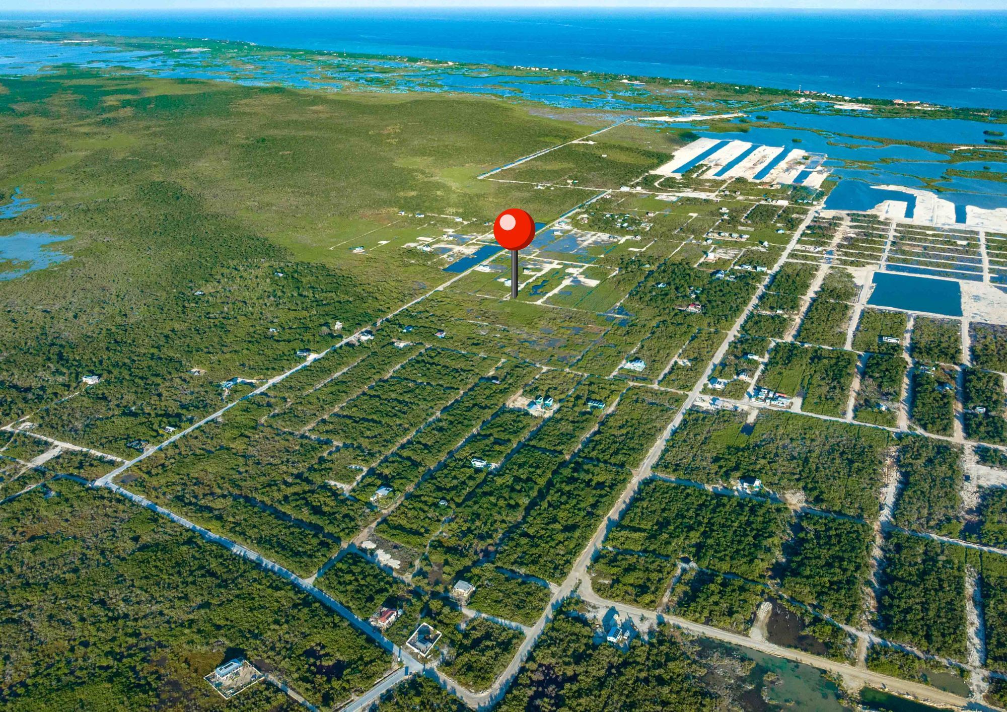 Aerial view of flat scrubland lots with sparse houses and a red map pin