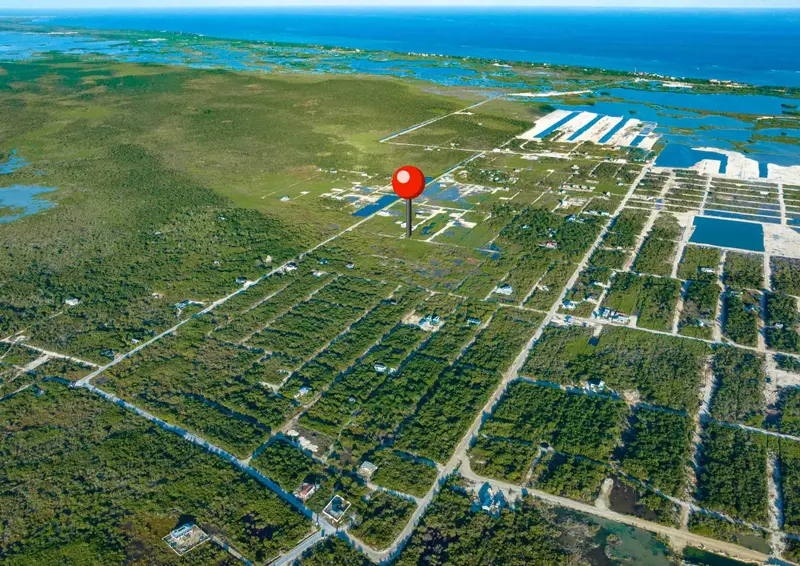 Aerial view of flat scrubland lots with sparse houses and a red map pin