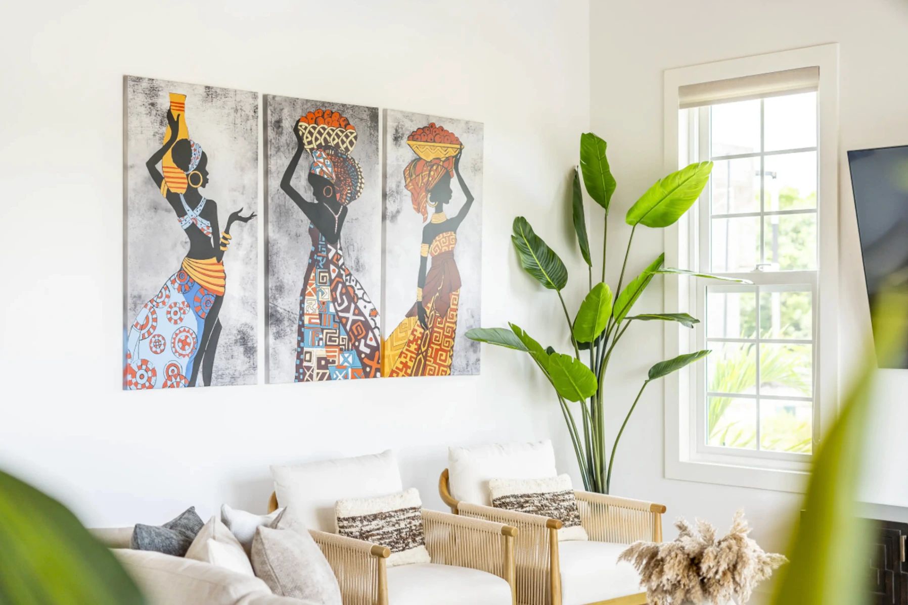 Living room with two-panel art of women carrying baskets, tall green plant, and cream rope chairs