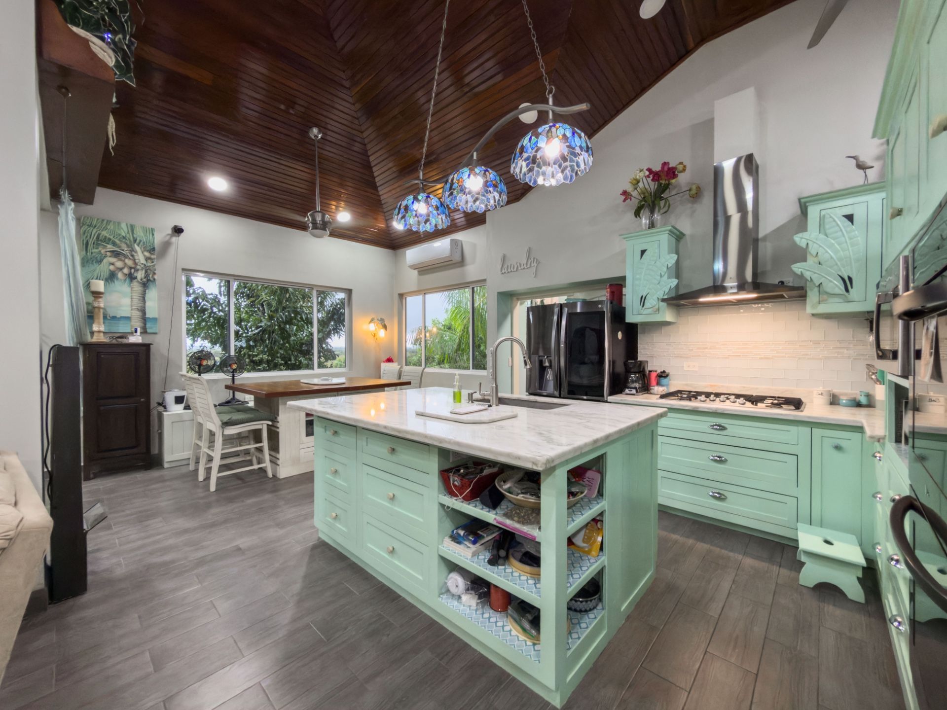 Kitchen island with mint green cabinets, marble top and blue mosaic pendant lights