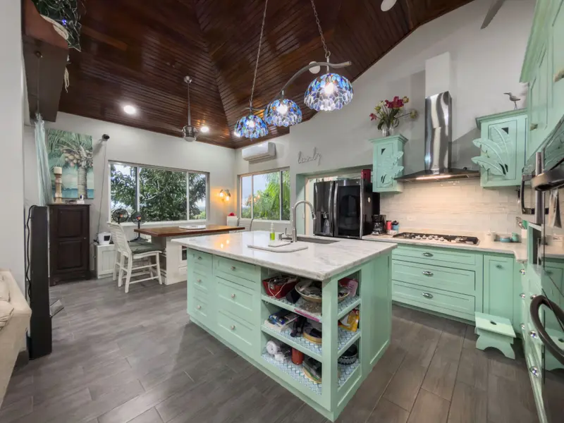 Kitchen island with mint green cabinets, marble top and blue mosaic pendant lights