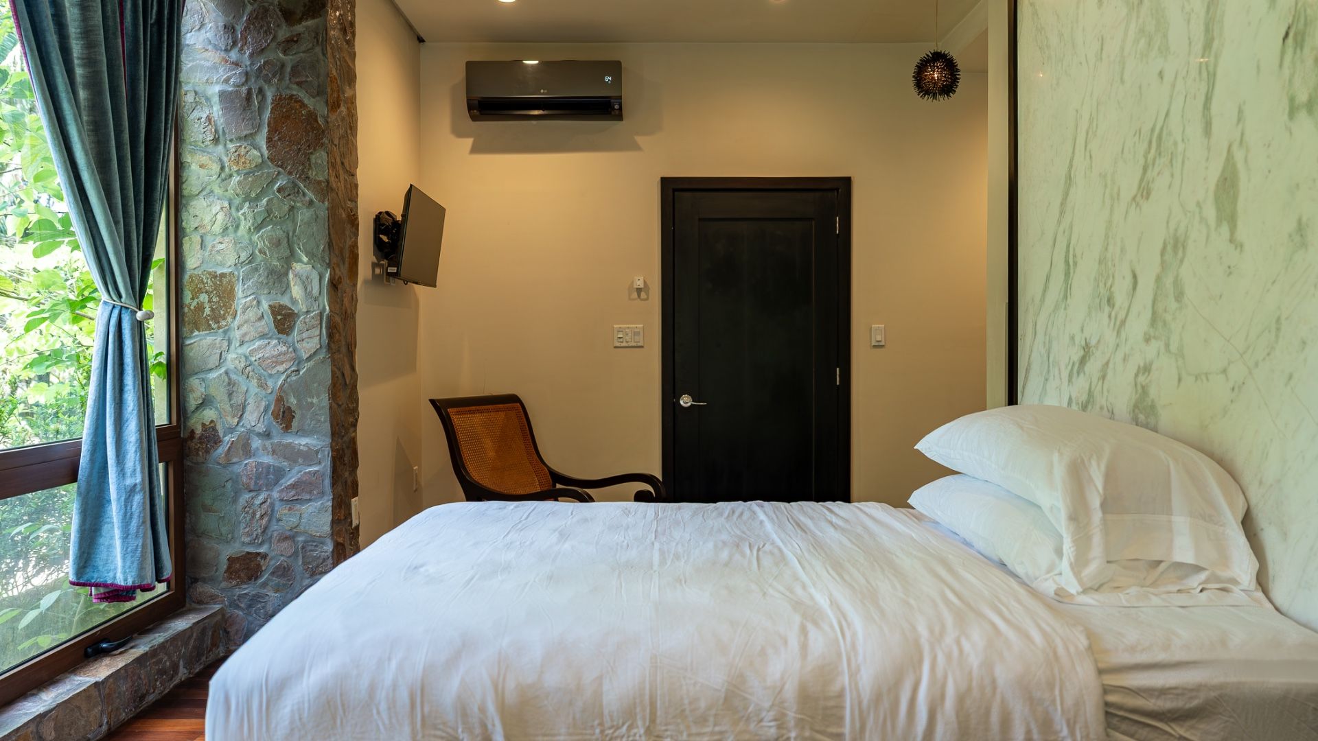 Bedroom with white bedding, cane armchair and dark wooden door