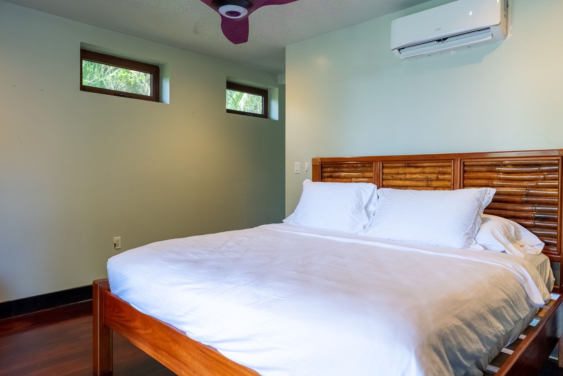 Bedroom with made bed, wooden headboard and maroon ceiling fan