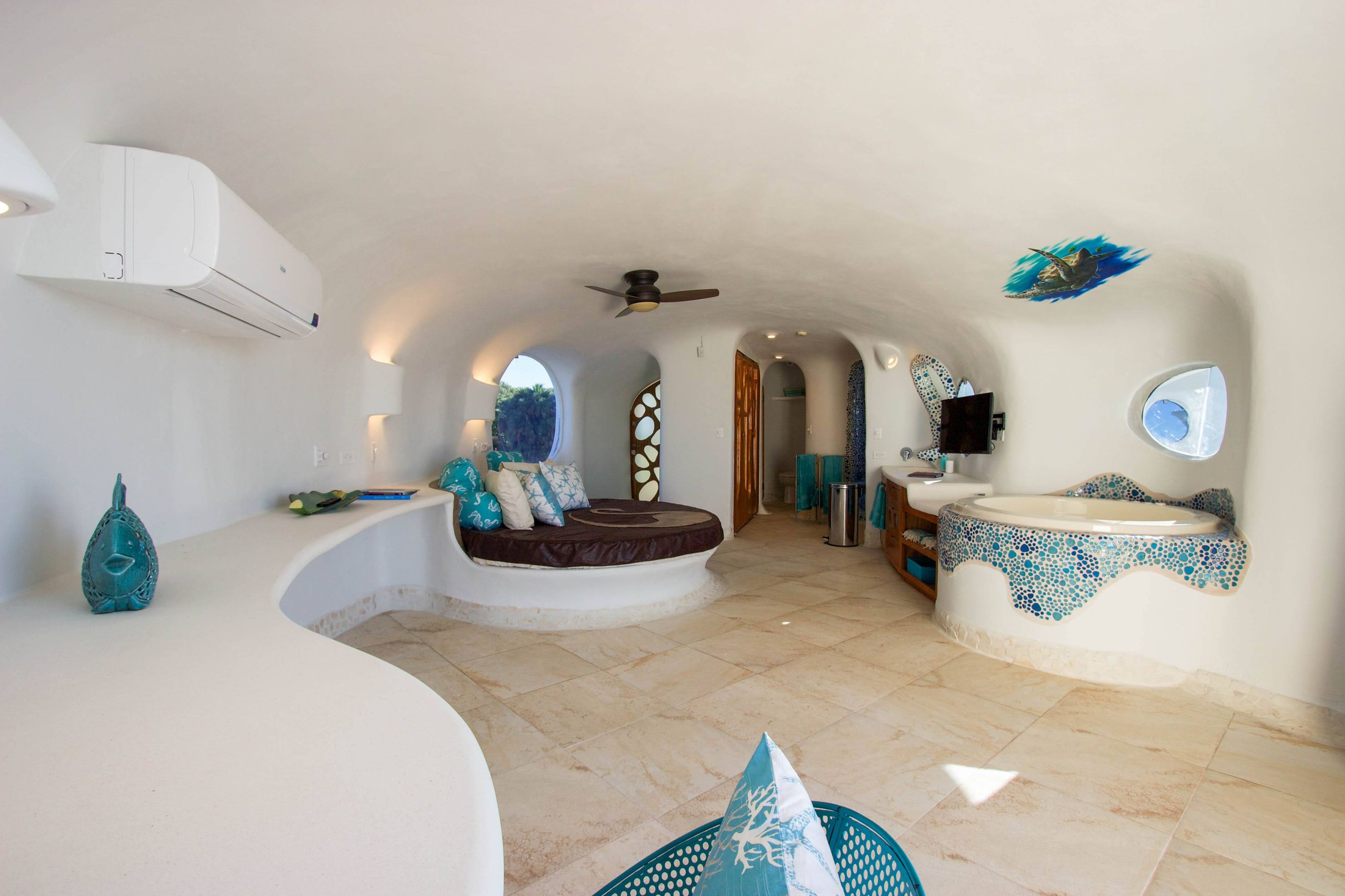 Round built-in bed with brown cushion and blue pillows in curved white room